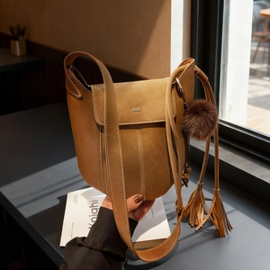Vintage caramel brown matte bucket bag with tassel and plush ball charm in a soft light setting