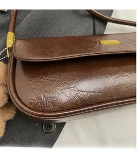 Detailed shot of brown baguette bag featuring glossy crinkled leather and gold buckle