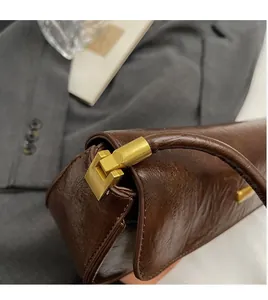 Macro shot of glossy brown leather handbag featuring sleek rectangular gold hardware detail