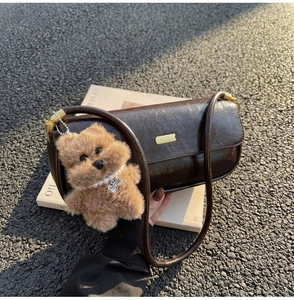 Detail of dark brown vintage leather handbag with gold bar trim and plush bear charm