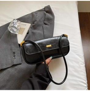 Detail of black glossy faux leather baguette bag with premium gold square hardware