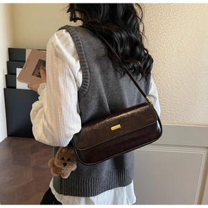 Detail of dark brown leather underarm bag with gold buckle and plush dog charm