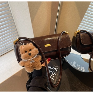 Macro detail of dark brown glossy leather bag with gold hardware and plush bear charm