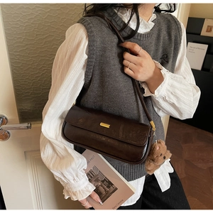 Detail of dark brown leather handbag with metallic clasp and cute plush bear charm