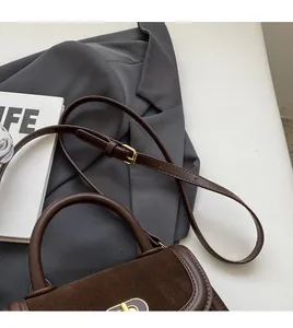 Vista dettagliata della borsa in pelle opaca marrone scuro con fibbia dorata e tracolla