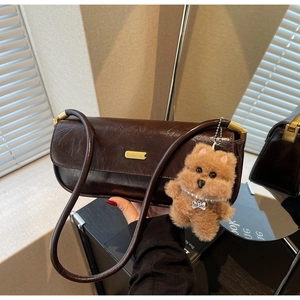Detail of dark brown vintage faux leather shoulder bag with gold clasp and plush dog charm
