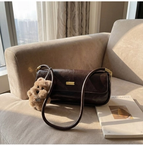 Detail of dark brown baguette bag featuring a gold plate and plush puppy charm