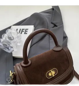 Dettaglio borsa in camoscio marrone con chiusura a scatto dorata e manico in pelle