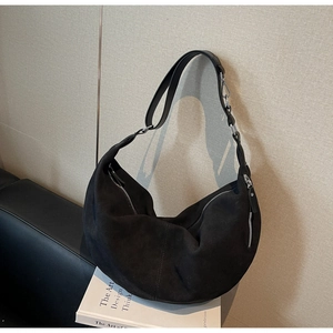 Close-up of black suede hobo bag with silver zipper and adjustable strap on books