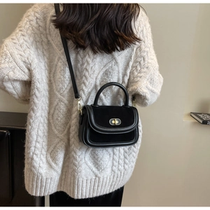Dettaglio della mini borsa nera con chiusura dorata indossata su un maglione a trecce crema