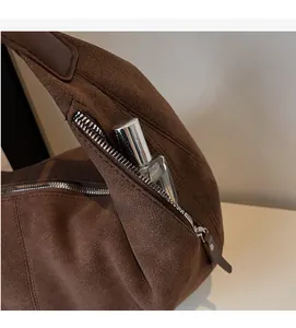 Detail view of the side zipper pocket on a brown suede shoulder bag with a perfume bottle