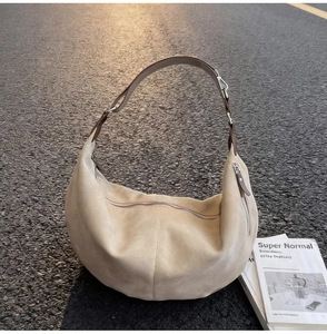 Detailed view of light beige suede crescent bag with metal buckles on textured ground