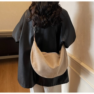 Detail of a large beige crescent bag showing suede texture and brown wide strap with buckle