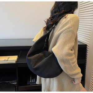 Side view of a black crescent shoulder bag worn with a beige sweater in a modern interior