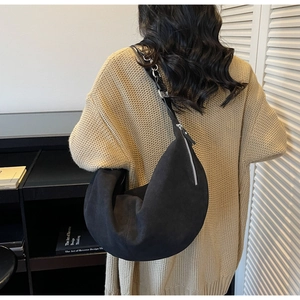 Detail of a large black hobo bag with a soft texture, styled with a beige knit sweater