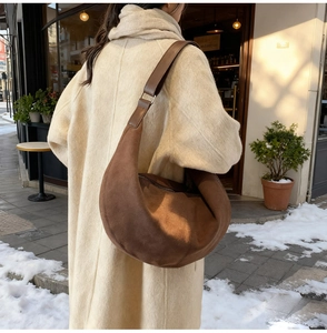 Brown suede hobo shoulder bag styled with a white winter coat in a snowy street scene