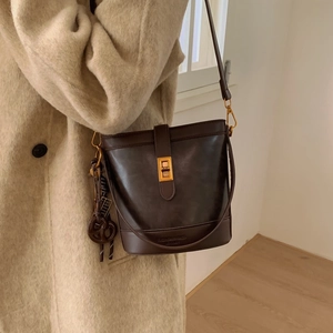 Sac seau en cuir marron foncé avec fermoir doré et pendentif tissé au look citadin