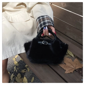 Détail du sac à main en fausse fourrure noire avec boucle et poignée tressée sur un banc