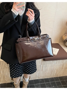 Detail of dark brown glossy leather tote bag with decorative buckle on a model