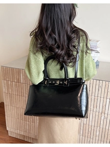 Detail showing the glossy black leather tote bag featuring gold buckle accents and top handles