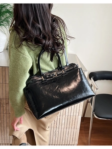 Detail of a large black glossy leather tote bag with a metal buckle and dual handles
