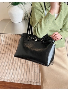Detail of large black patent leather tote bag with metal buckles and retro shoulder strap