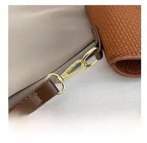 Close-up of golden metal hook on brown leather strap and woven caramel texture handbag