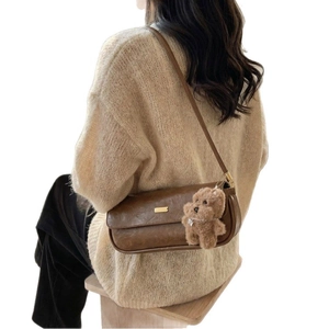 Brown leather baguette bag with gold buckle and teddy bear charm shown on shoulder