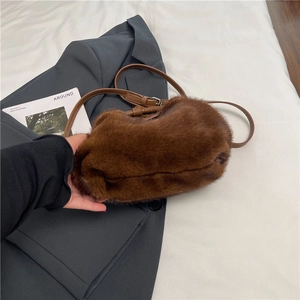 Détail d'un sac bandoulière en peluche marron avec sangle en cuir sur un blazer gris