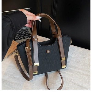 Detail of a black woven handbag with brown leather straps and gold metal hardware