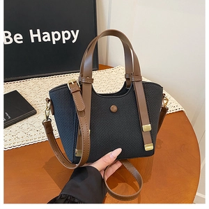 Detail of black woven tote bag with brown leather handles and golden metal buckle