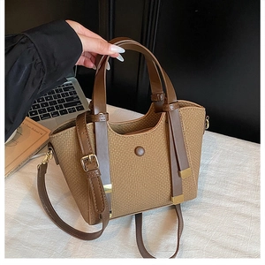 Detail of a brown woven tote bag with leather straps and gold metal hardware accents