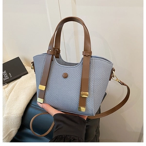 Close-up of light blue woven tote bag with brown leather handles and gold metal buckle