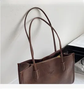 Detail of dark brown tote bag with slim handles and embossed logo by a white wall