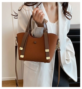 Detail of brown woven texture handbag with gold hardware worn by a model in a white blazer