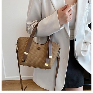 Brown woven tote bag detail showing leather handles and gold hardware on model