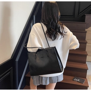 Detailed view of black PU leather tote bag with subtle texture carried by a model