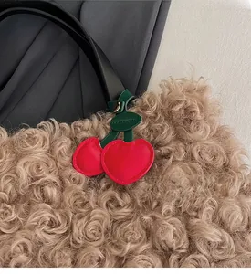 Close-up of red heart cherry bag charm with green leaves on fuzzy brown bucket bag