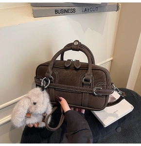 Detail of dark brown matte box bag with white contrast stitching and plush rabbit charm