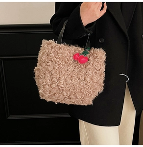 Detail of plush bucket bag in light brown faux fur with red cherry charm accessory