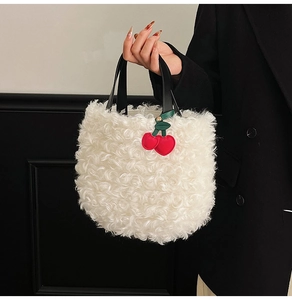 Close-up of white faux fur bucket bag with black leather handle and red cherry charm