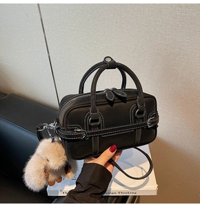 Detailed view of a black Boston bag featuring white contrast stitching and a plush rabbit charm