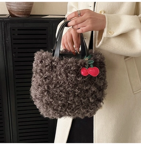 Detailed texture of grey plush tote bag with black leather handle and red cherry charm