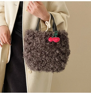 Detail of grey curly faux fur tote bag with cherry charm accessory and black handle