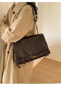 Detail der dunkelbraunen Leder-Schultertasche mit Goldverschluss auf beigem Trenchcoat