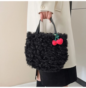 Detail of black faux fur tote bag featuring a bright red cherry charm accessory