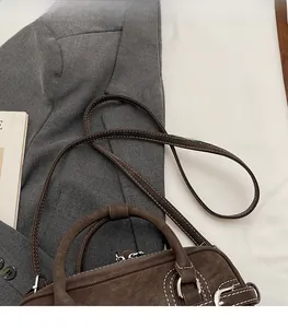 Detailed view of dark brown suede bag with white stitching and silver hardware accents
