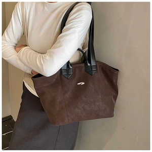 Detail der dunkelbraunen matten Leder-Tote-Bag mit Metall-Logo auf hellem Pullover