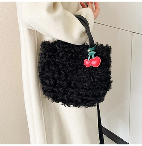 Detail of black faux fur bucket bag with plush texture and decorative cherry charm