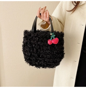 Close-up of black curly plush handbag with cute red cherry charms and leather handle